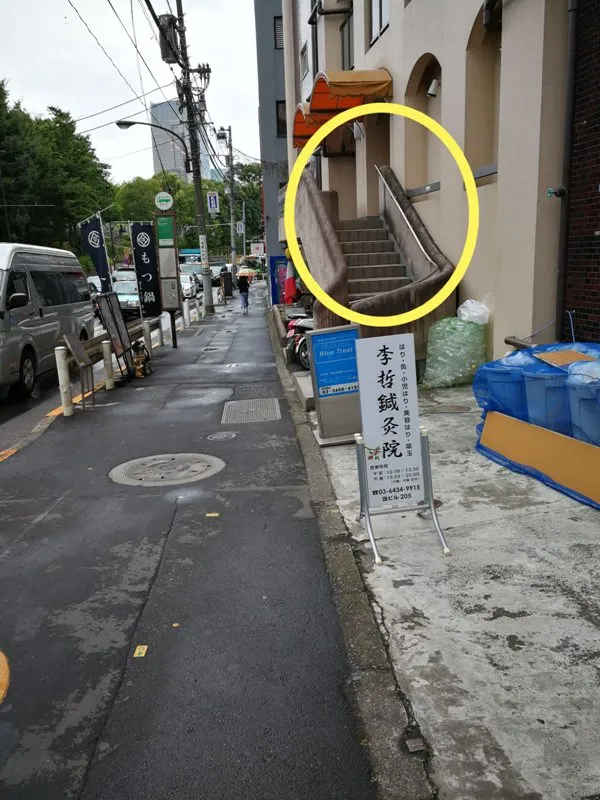 李哲鍼灸院の看板と、黄色い丸で囲まれたビル入口の階段