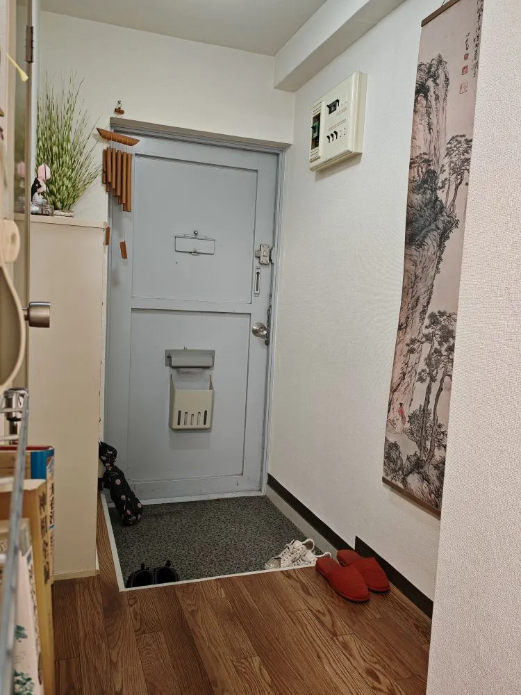 マンション入口に並ぶ患者の靴と傘、中国山水画の掛け軸、スリッパと靴棚の飾り物が写っている。