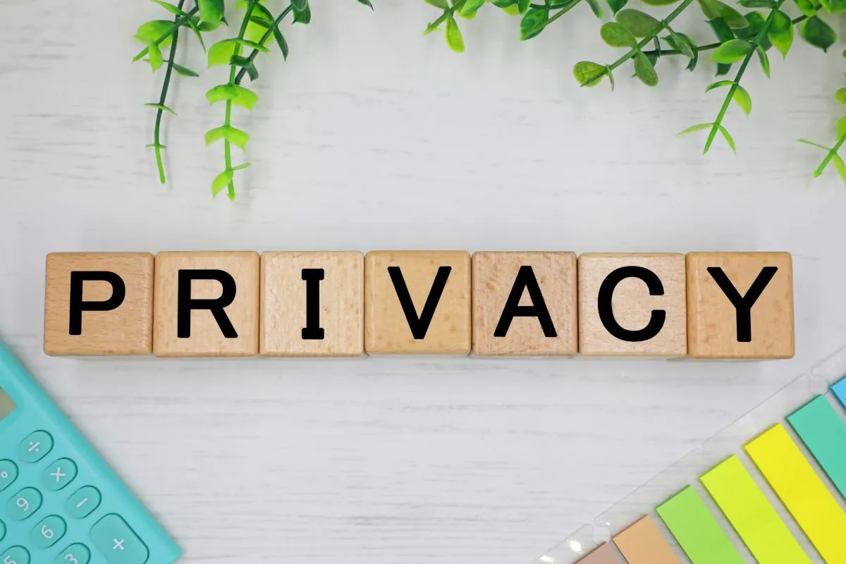 木製ブロックで並べた「PRIVACY」の文字と緑の葉、電卓、付箋が置かれたプライバシー保護をイメージした写真